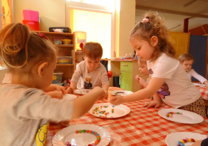 Dzieci układają kolorowe cukierki na brzegu talerzyków.